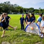 Students practicing soccer with a small goal on the grass.
