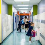 Students and a teacher in a school hallway lined with lockers.