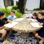 Four students writing at an outdoor picnic table.